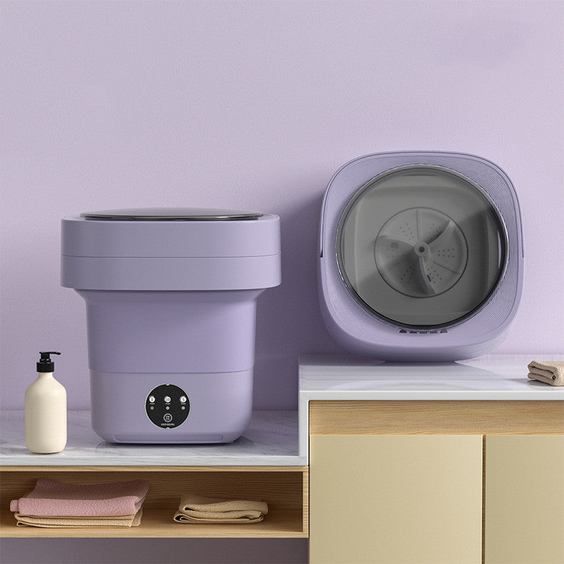 Purple foldable washing machine open on a marble counter beside a second unit showing the grey spin drum
