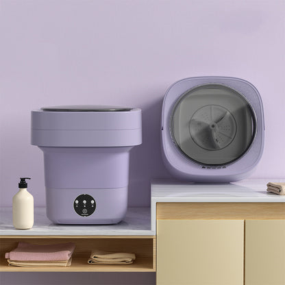 Purple foldable washing machine open on a marble counter beside a second unit showing the grey spin drum