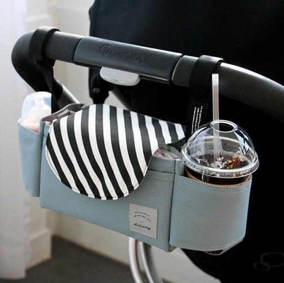 Blue and white striped stroller organiser bag mounted on a stroller handlebar with a drink in the cup holder