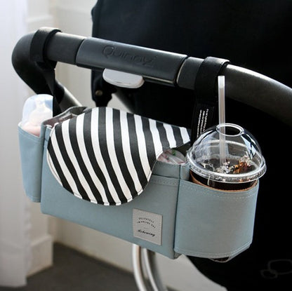 Blue and white striped stroller organiser bag mounted on a stroller handlebar with a drink in the cup holder