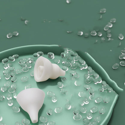 Two detachable white silicone nozzle tips on a green dish surrounded by water droplets