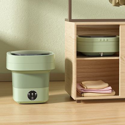 Green foldable washing machine on a wooden floor beside a cabinet, with a second unit collapsed flat on the shelf above