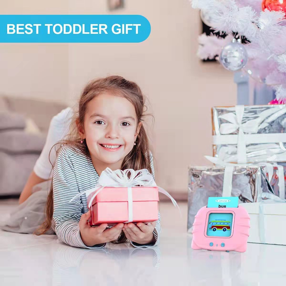 Young girl holding a wrapped gift beside the pink talking flash card machine at Christmas, shown as a toddler gift idea