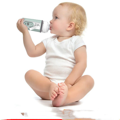 Baby sitting and drinking from a bottle held in the green warming sleeve