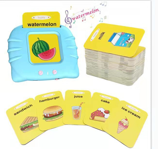 Blue talking flash card machine reading the word watermelon aloud, beside a stack of yellow food cards including sandwich, hamburger, juice, cake and ice cream