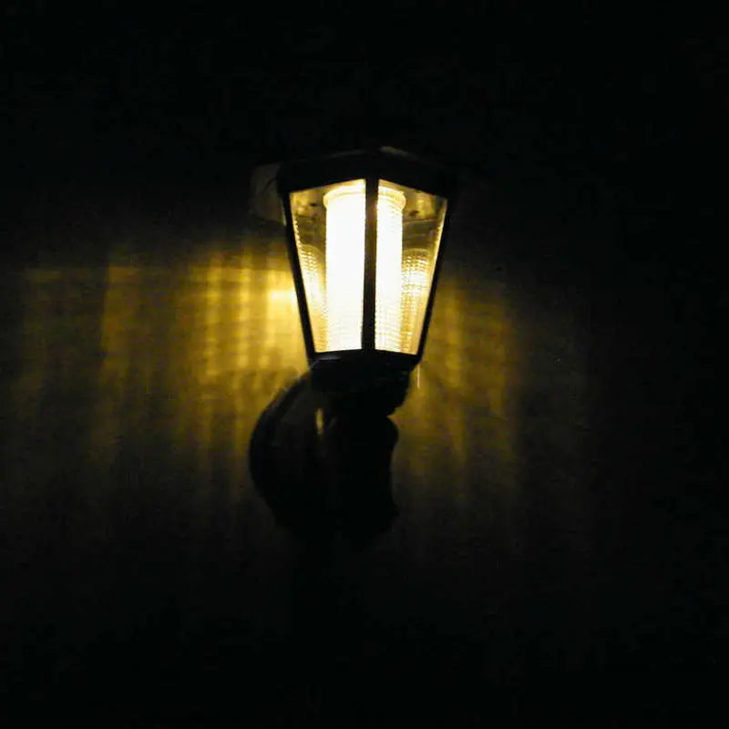 Solar hexagonal outdoor wall light mounted glowing warm on a wall at night