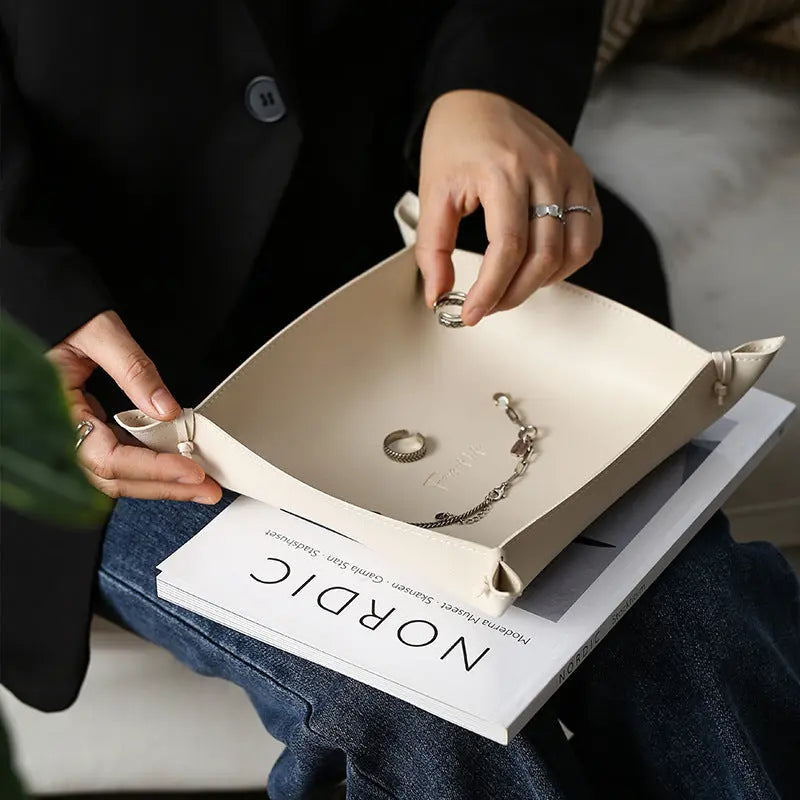 Hands placing jewelry into a leather storage tray styled with a book