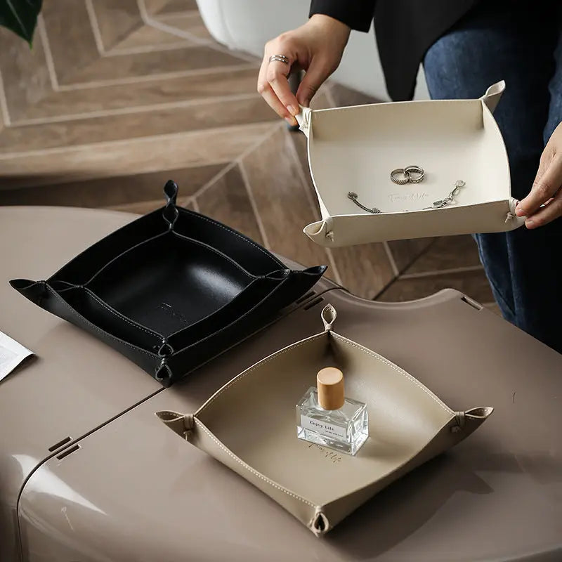 Leather storage trays styled with hands, a perfume bottle, and jewelry on a desk