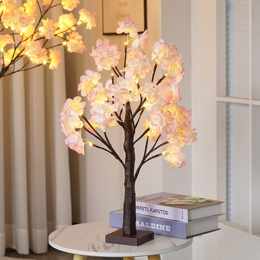 LED cherry blossom tree light glowing warmly on a bedside table with books