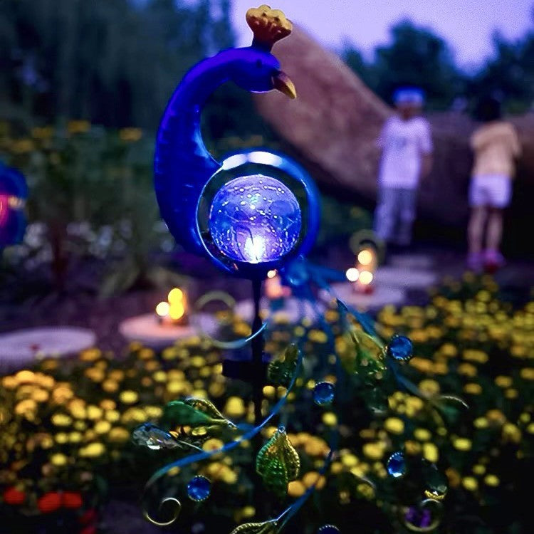 Solar metal peacock garden lamp glowing at dusk on a patio with string lights