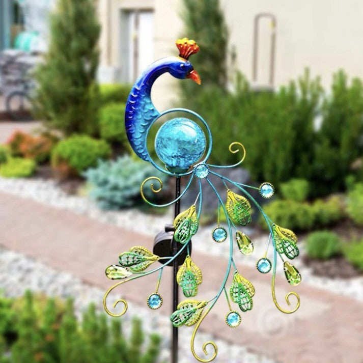 Solar metal peacock garden lamp styled against a house with greenery