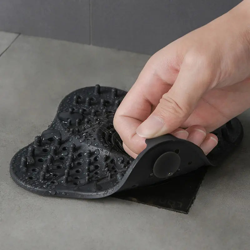 Hand holding a silicone drain hair catcher to show scale and suction cup base