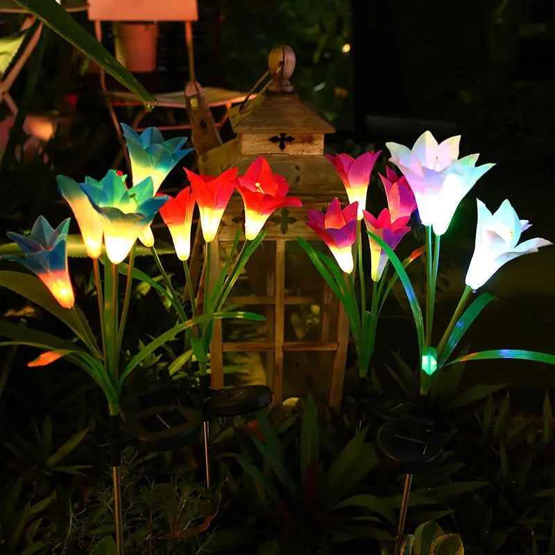 Solar-powered lily-shaped garden stake light glowing softly in a dark garden at night