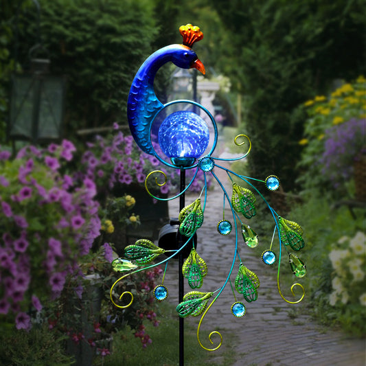 Solar metal peacock garden lamp stake light among purple flowers on a garden path